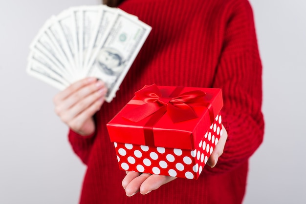 Person holding red present box and stack of cash in hands