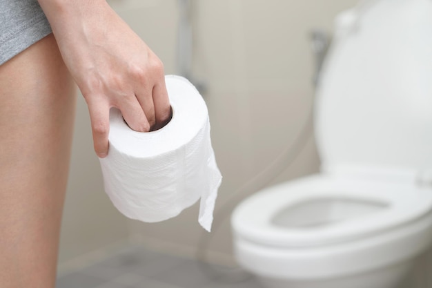 A person holding a roll of toilet paper in front of a toilet seat.