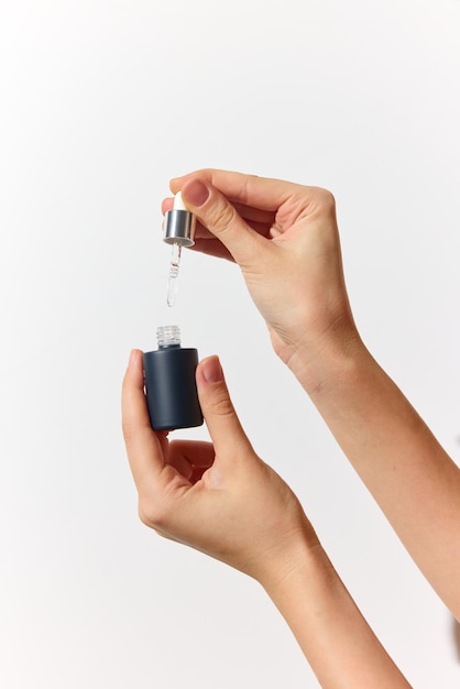Person holding small bottle with dropper on white background hand holding bottle in other hand