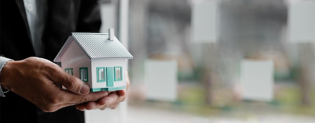 小さな家のモデルを持っている人不動産業者は家を提供します財産保険とセキュリティの概念ボケ味の背景のコピースペースを持つ広いバナー構成
