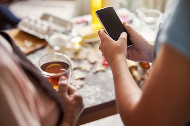 Persona in possesso di uno smartphone vicino al tavolo della cucina ricoperto di farina