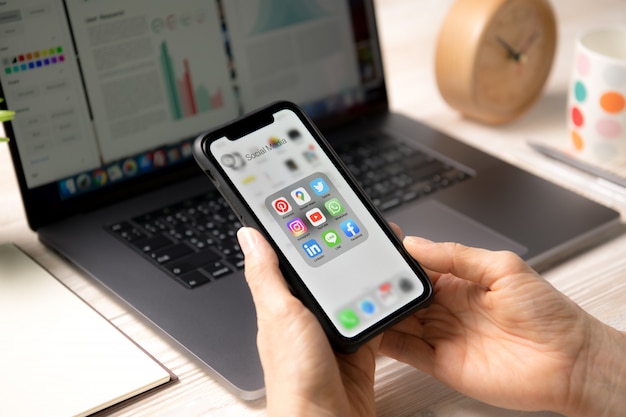 Person holding a smartphone with icons of social media on the screen at home