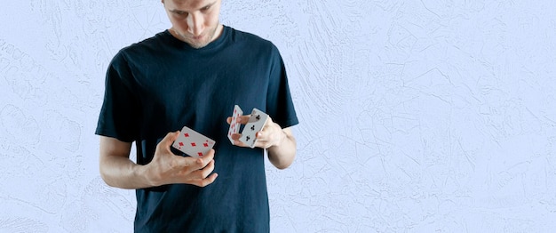 A person holding some playing cards and doing the magic trick focus, standing angaist the wall wide webn banner
