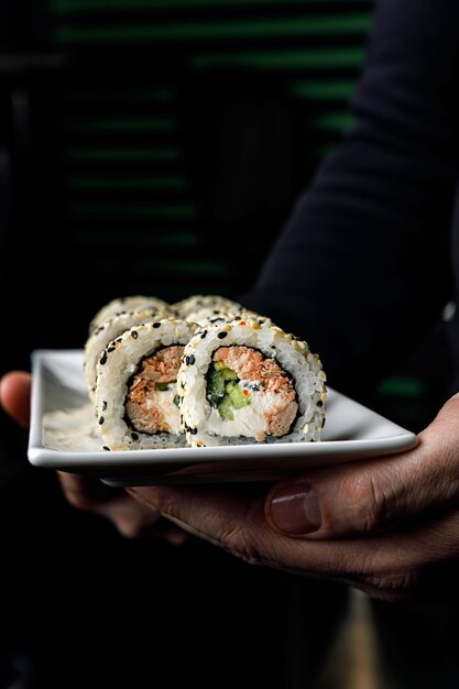 A person holding a sushi roll with a green top