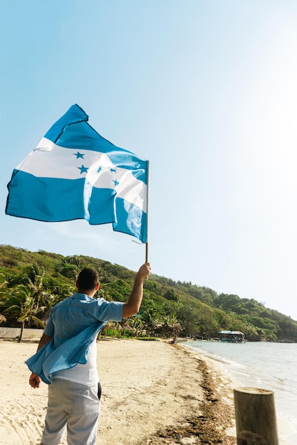 A person holding and waving honduras flag in a beach Patriotism concept