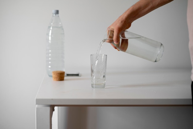 A person holds a bottle and pour water in the glass