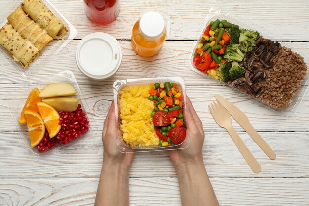 Person holds box with takeaway food on wooden background, top view