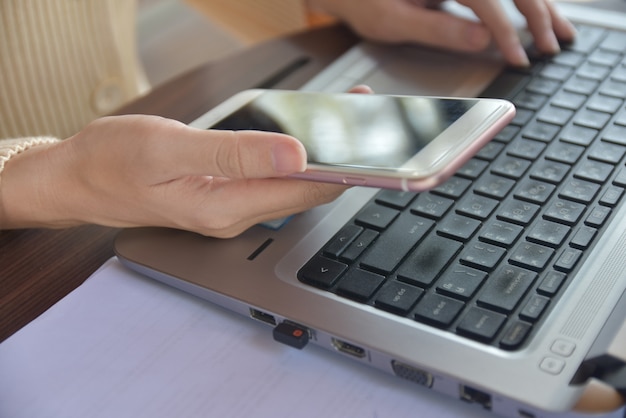 Person holds cell phone and uses the laptop