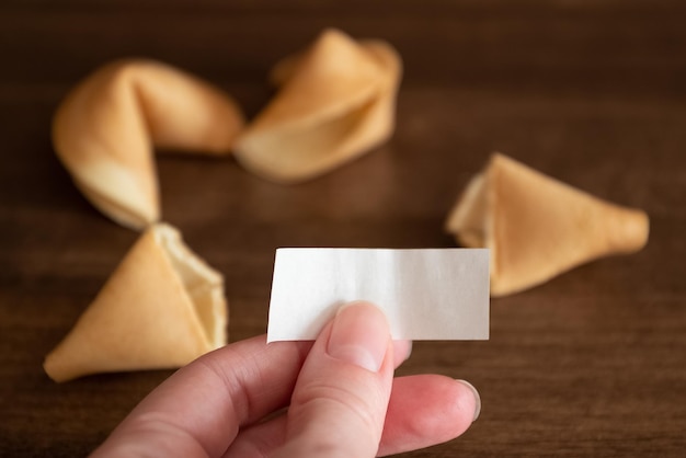 Person holds in hand blank paper slip from fortune cookie against few cookies mockup for your wishes