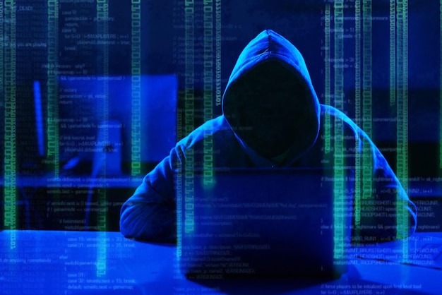 person hoodie or hacker with code overlay of cybersecurity problem with coding graphic for cybercrime programmer night and software update on laptop with hacking expert writing algorithm system