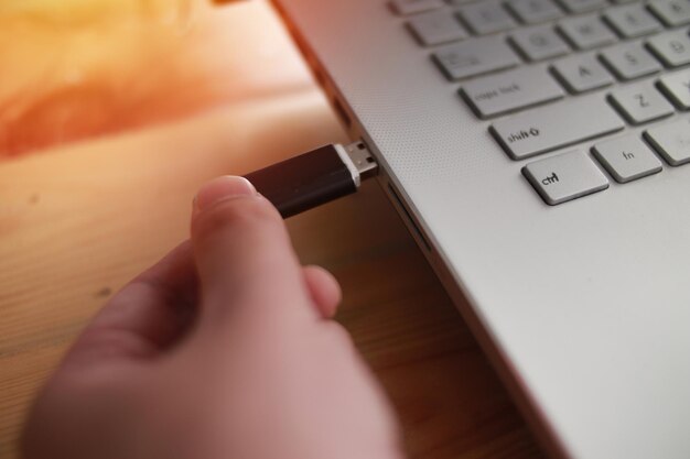 Person inserting plug in flash disk into usb port in laptop personal computer data transfer device