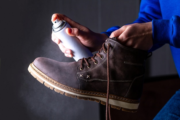 Человек моет и распыляет средство на мужские замшевые повседневные ботинки для защиты от влаги и грязи. Чистка обуви