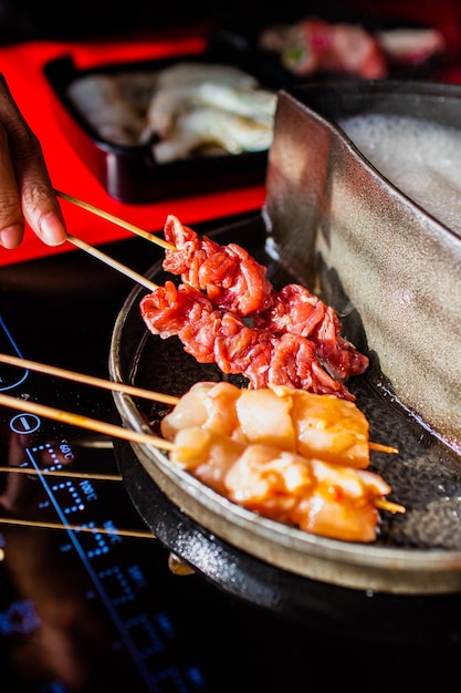 A person is cooking meat on a stick with a stick that says'noodle'on it