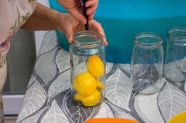A person is holding a knife and a jar of lemons on a table.