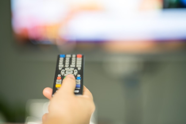 A person is holding a remote with a yellow, red, and blue button.