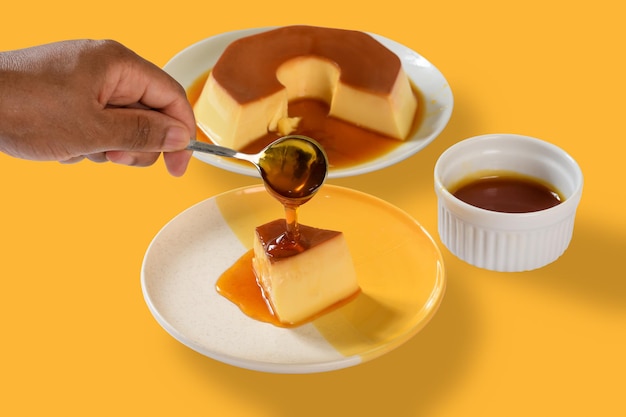 A person is holding a spoon over a plate of flan and sauce.