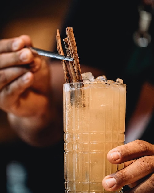 A person is holding a straw and a glass of the drink with cinnamon sticks on it