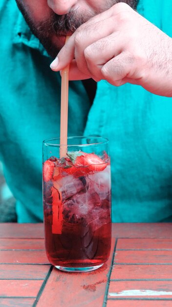 Photo a person is holding a straw in a glass with strawberries and strawberries