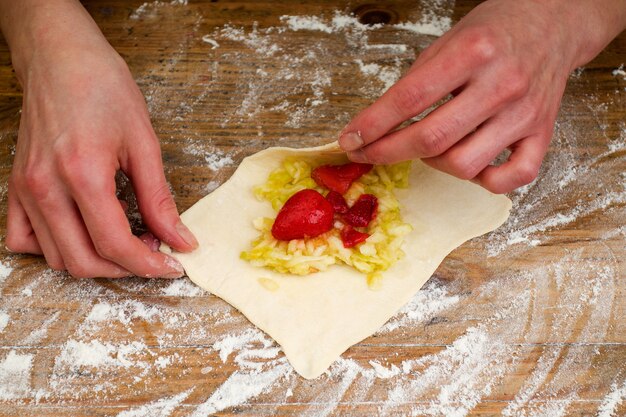 Person is making pastry with strawberries and apple