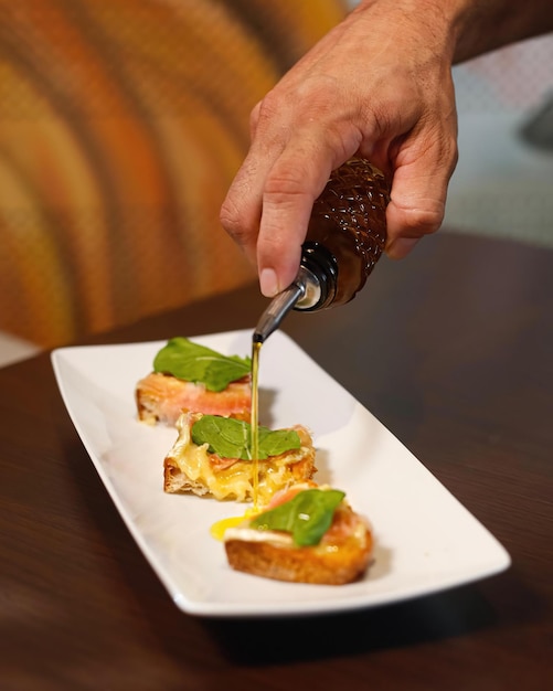 A person is pouring a sauce onto toast with a fork.