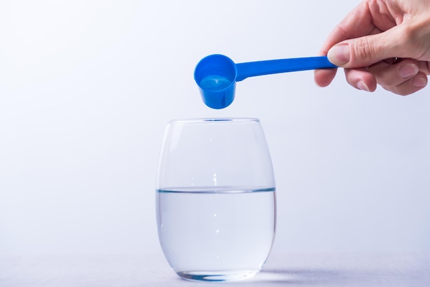 A person is pouring water into a glass with a blue spoon.