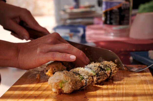 Photo a person is preparing a homemade japanese sushi meal cutting fresh rolls on the board with a sharp knife