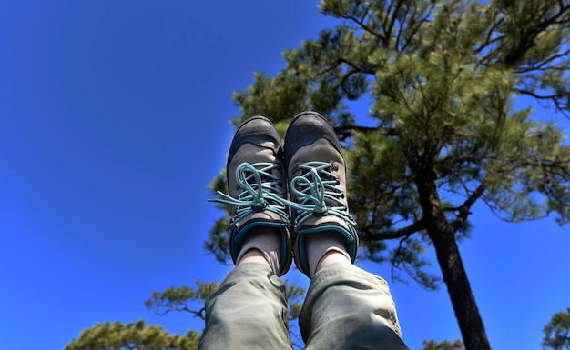 A person is raising his or her leg with shoe to blue sky with a blur pine tree in background