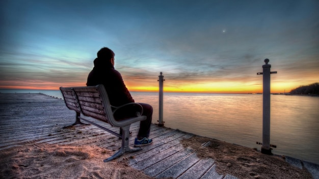 a person is sitting on a bench and looking at the water