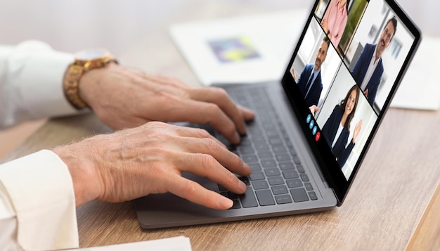 A person is typing on a laptop during a video conference meeting with four other people the laptop
