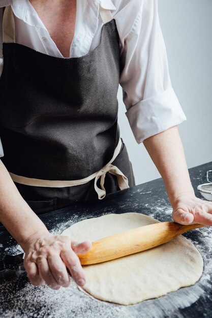 A person on kitchen rolling a pastry with the pin