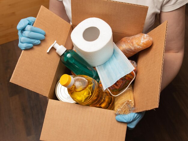 Person in latex gloves has holding a box with donation goods Food delivery service