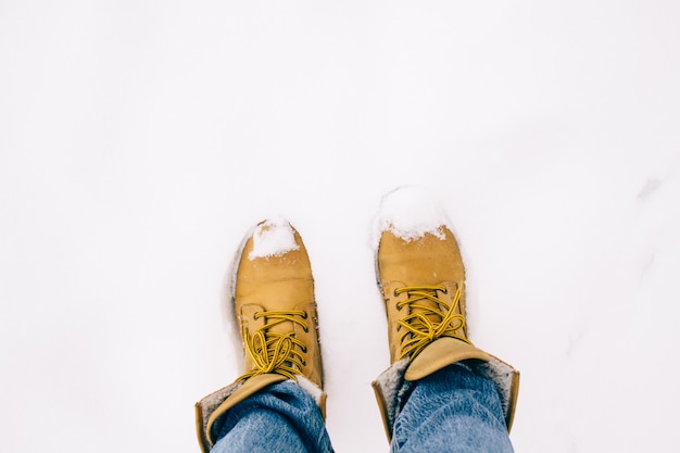 Gambe della persona in stivali gialli con blue jeans sulla neve, l'inverno sta arrivando