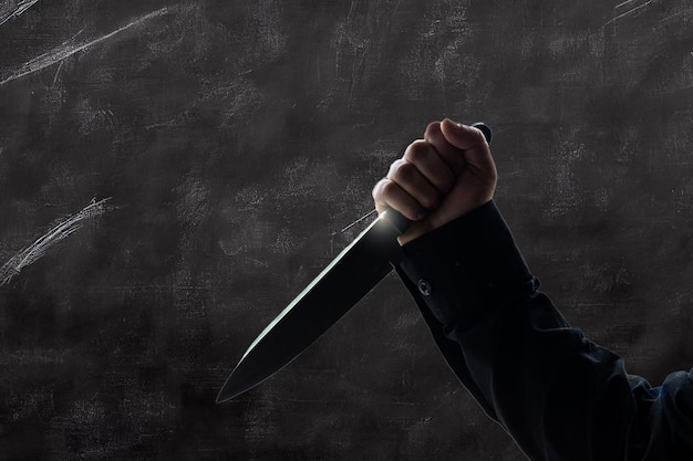 Person in long sleeved black shirt holding a knife against a gray background