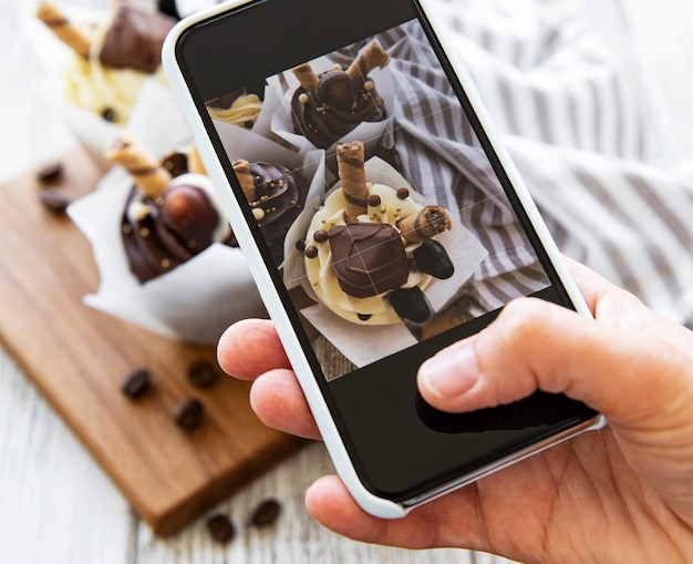 Foto la persona fa una foto di cupcakes su uno smartphone