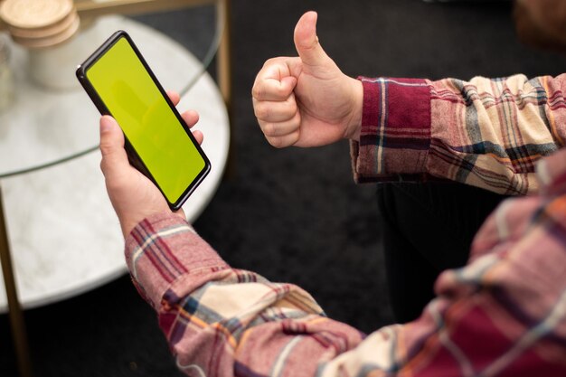 Person making like gesture front cell phone with chroma key green screen in living room with copy space