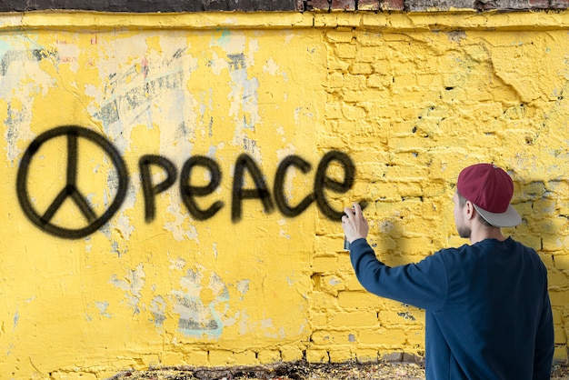 A person male write with spray paint can the stop war statement on the wall, graffiti symbol concept