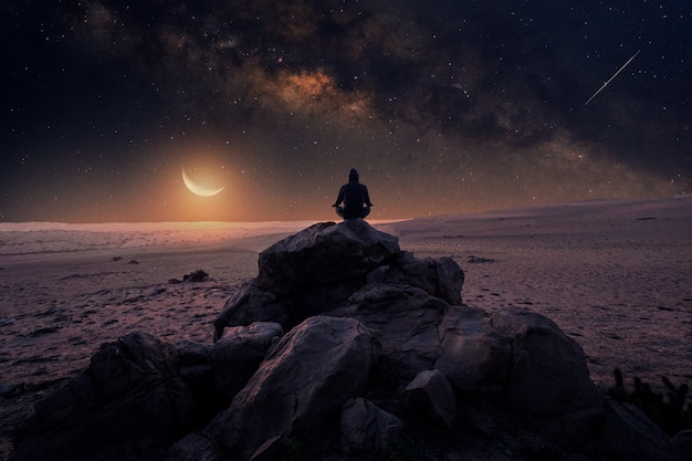 person meditating on the mountain under the stars with Milky Way and Moon in the background