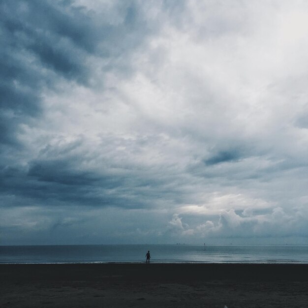 写真 雲の空を背景にビーチにいる人