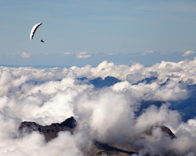Человек, катающийся на параплане над облачным пейзажем на фоне голубого неба в швейцарских Альпах