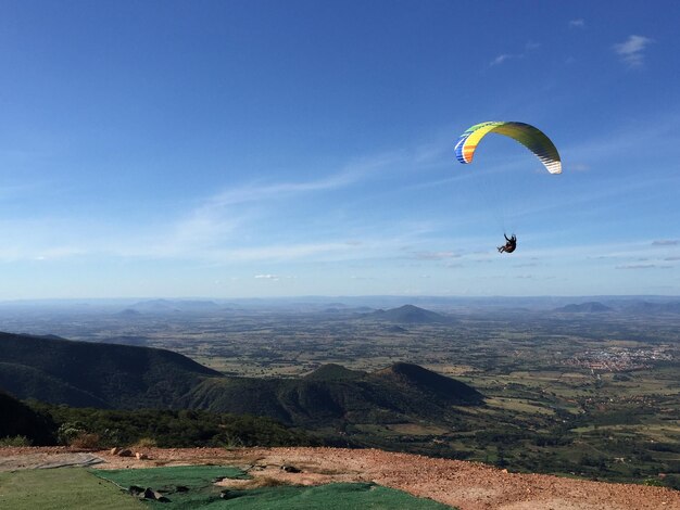 Person paragliding over mountain against sky