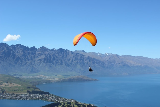 Person paragliding over mountains against blue sky