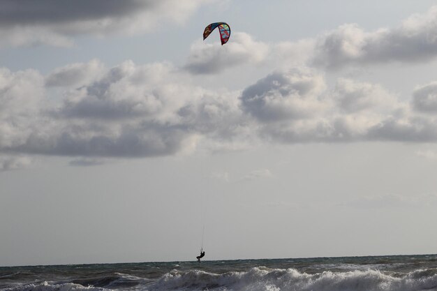 Person paragliding over sea against sky