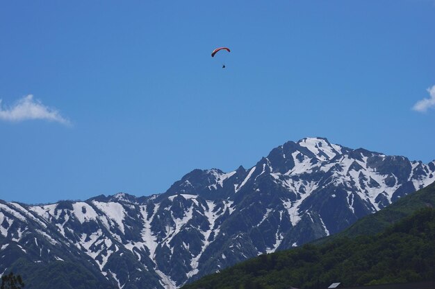 Person paragliding over snowcapped mountain against sky