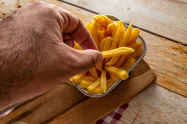 Person picking up a french fry on a basket full of french fries on rustic wooden table