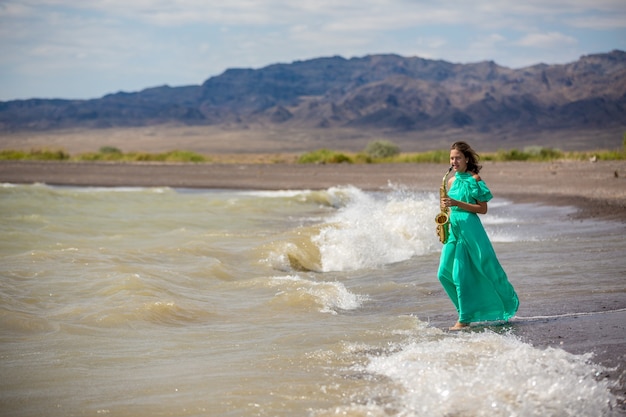 Person playing the saxophone sitting on the rocks in front of a beautiful sea