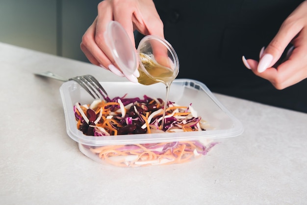 A person pouring a sauce into a container of salad.