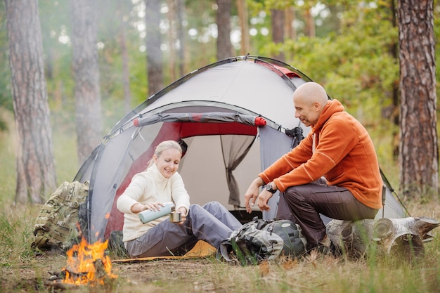 A person pouring tea from a thermos into his friends cup while camping