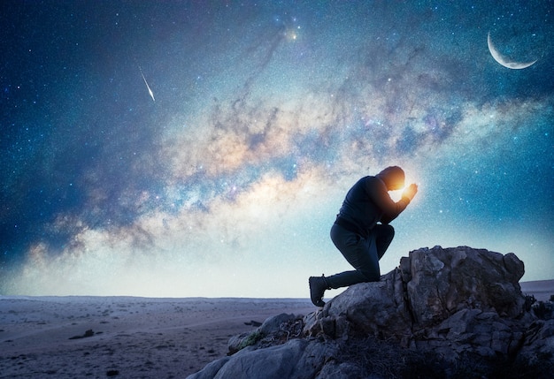 person praying or meditating at night under the Milky Way and Moon