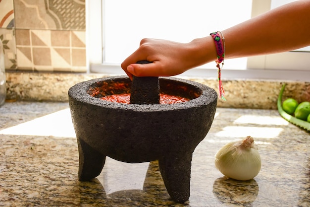 A person preparing a red spicy Mexican sauce in a traditional molcajete