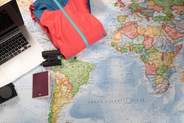 Person preparing trip with laptop, binocular, jacket and passport on a worldwide map.